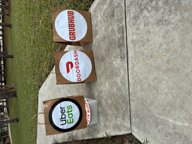 The Elevated Delivery Platform in action, holding Grubhub, DoorDash, and Uber Eats bags off the ground at a customer's door.